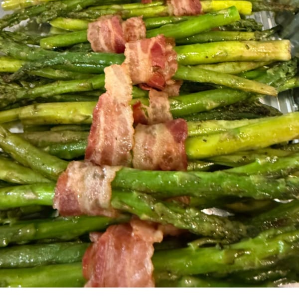 Cooked green asparagus spears wrapped with crispy bacon strips, arranged in rows.