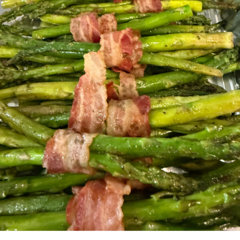 Cooked green asparagus spears wrapped with crispy bacon strips, arranged in rows.