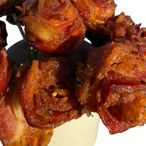 Crispy, golden-brown candied bacon pieces on skewers, served in a white cup.