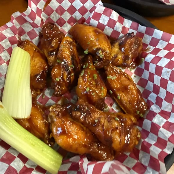 Phat Daddy's BBQ chicken wings with sauce and green onions, served with celery sticks.