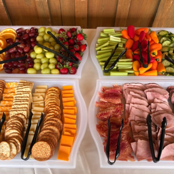 A buffet spread featuring trays of fresh fruit, vegetables, crackers, cheese, and deli meats.
