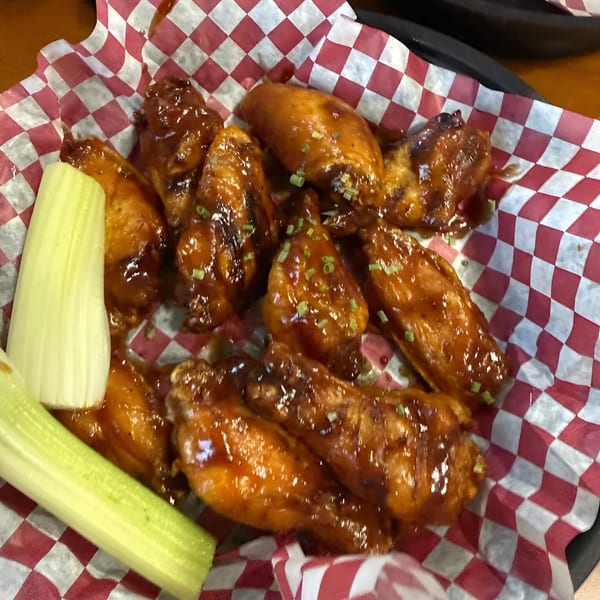 Phat Daddy's BBQ chicken wings with barbecue sauce and chopped green onions, served with celery sticks.