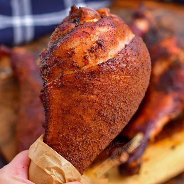Hand holding a large, perfectly smoked Phat Daddy's BBQ turkey leg wrapped in brown paper.