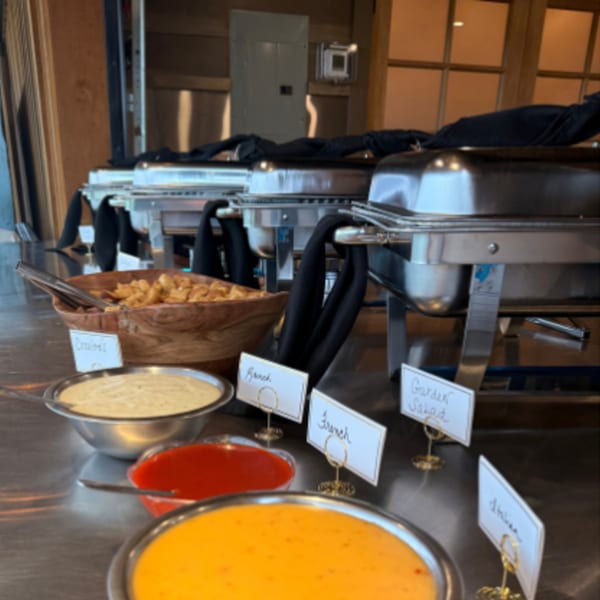 Buffet line with chafing dishes, salad dressings, and croutons on a stainless steel counter.