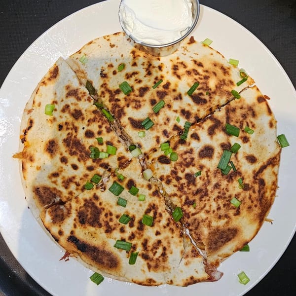Phat Daddy's BBQ quesadilla, cut into wedges, topped with green onions, and a side of sour cream.