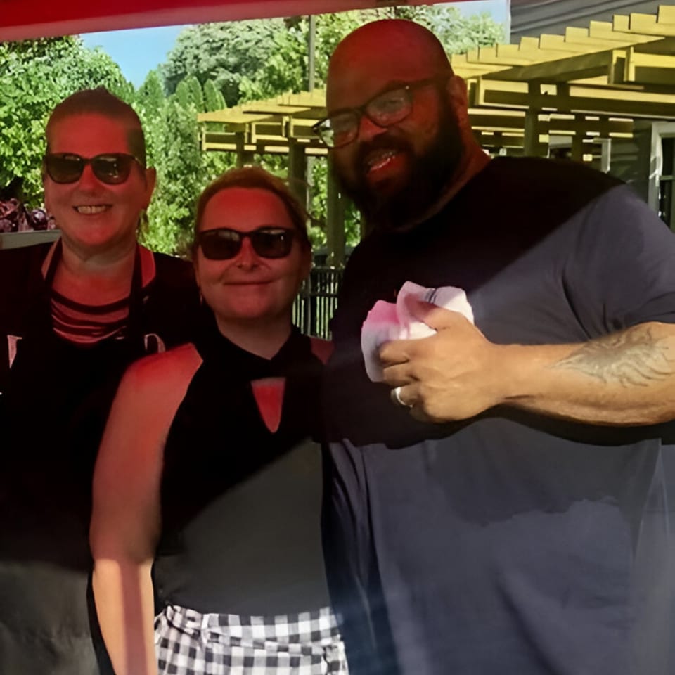 Three Phat Daddy's BBQ staff members, two women and one man, smiling outdoors.