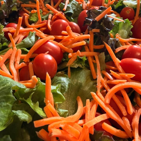Fresh garden salad with green lettuce, red cherry tomatoes, and shredded orange carrots.
