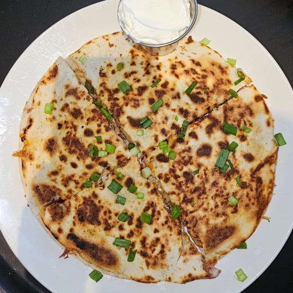 Phat Daddy's BBQ quesadilla, cut into wedges, topped with green onions, served with sour cream.